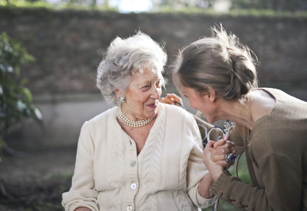 nurse talking to a seated elderly women with dementia outdoor