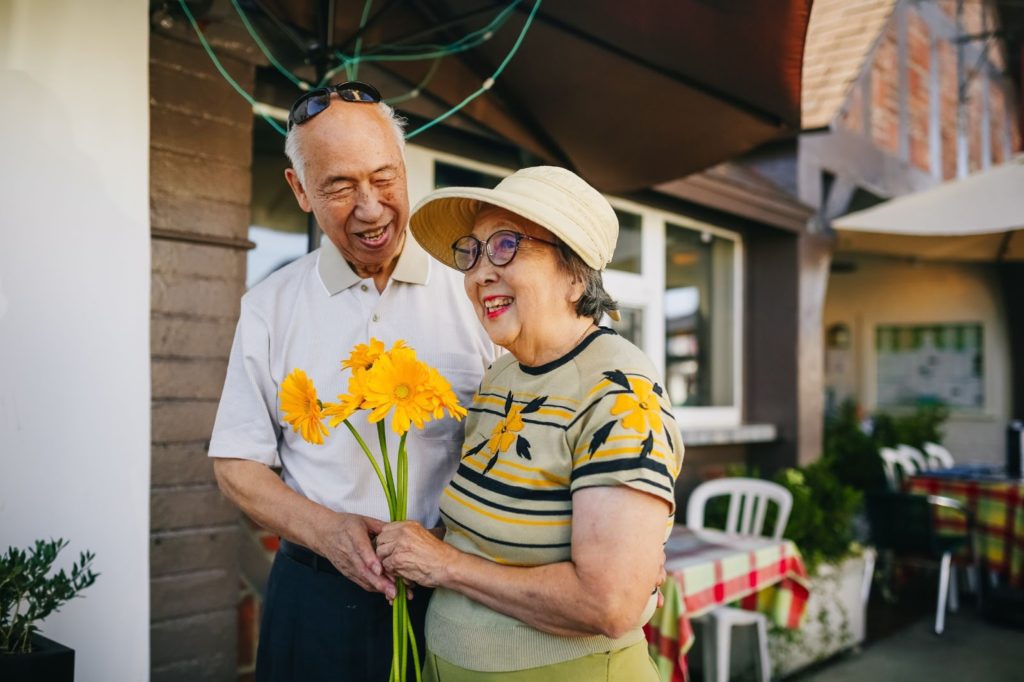 elderly couple holding flowers together outside