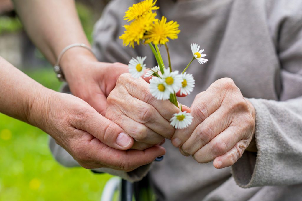 patient advocate taking care of elder holding flowers outside
