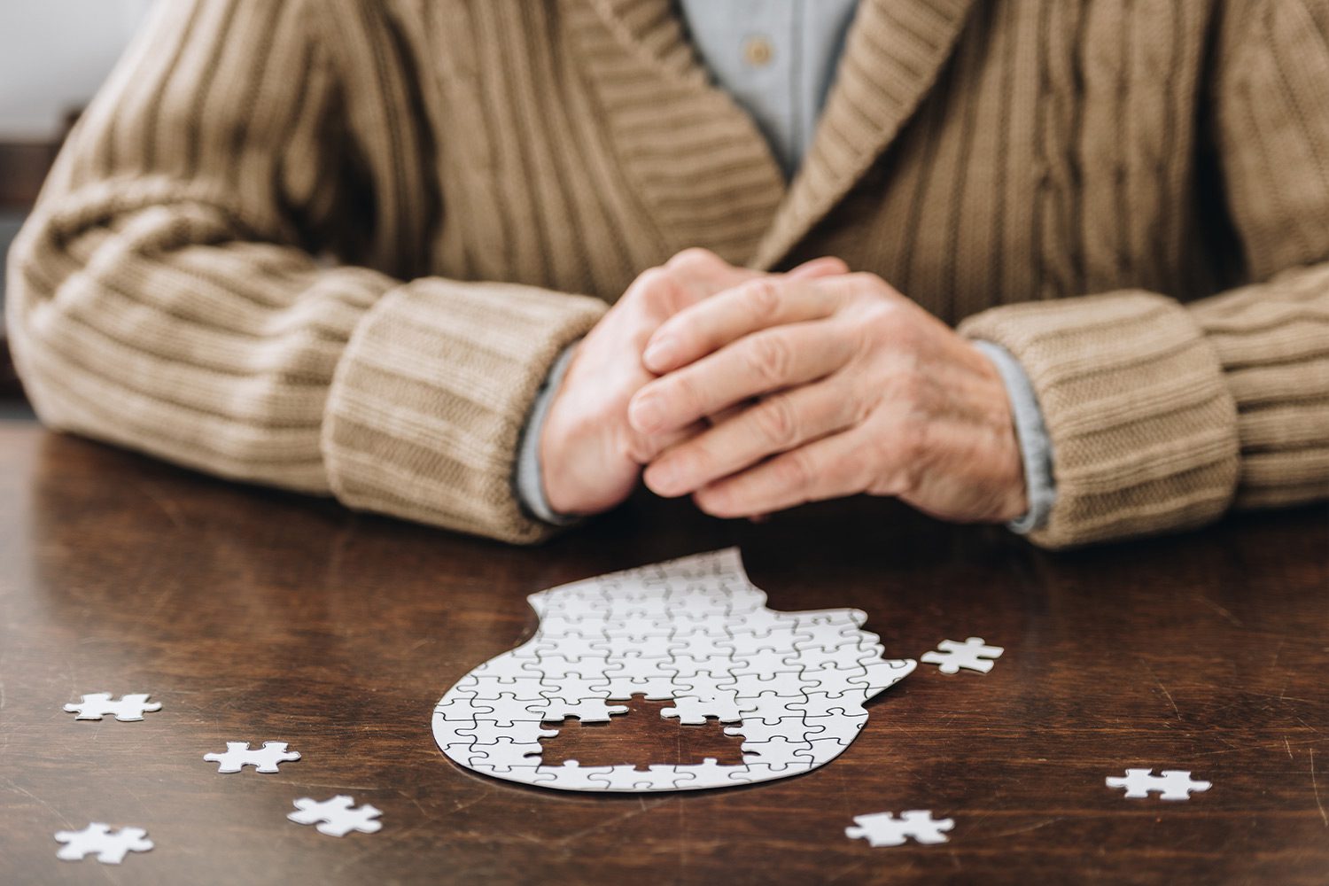 senior suffering from dementia solving head shaped puzzle on wooden table