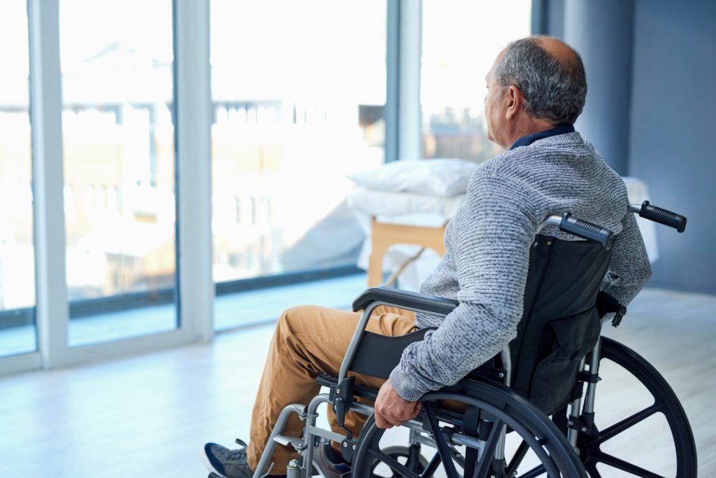 man in a wheelchair at a skilled nursing facility looking thoughtfully out of a window