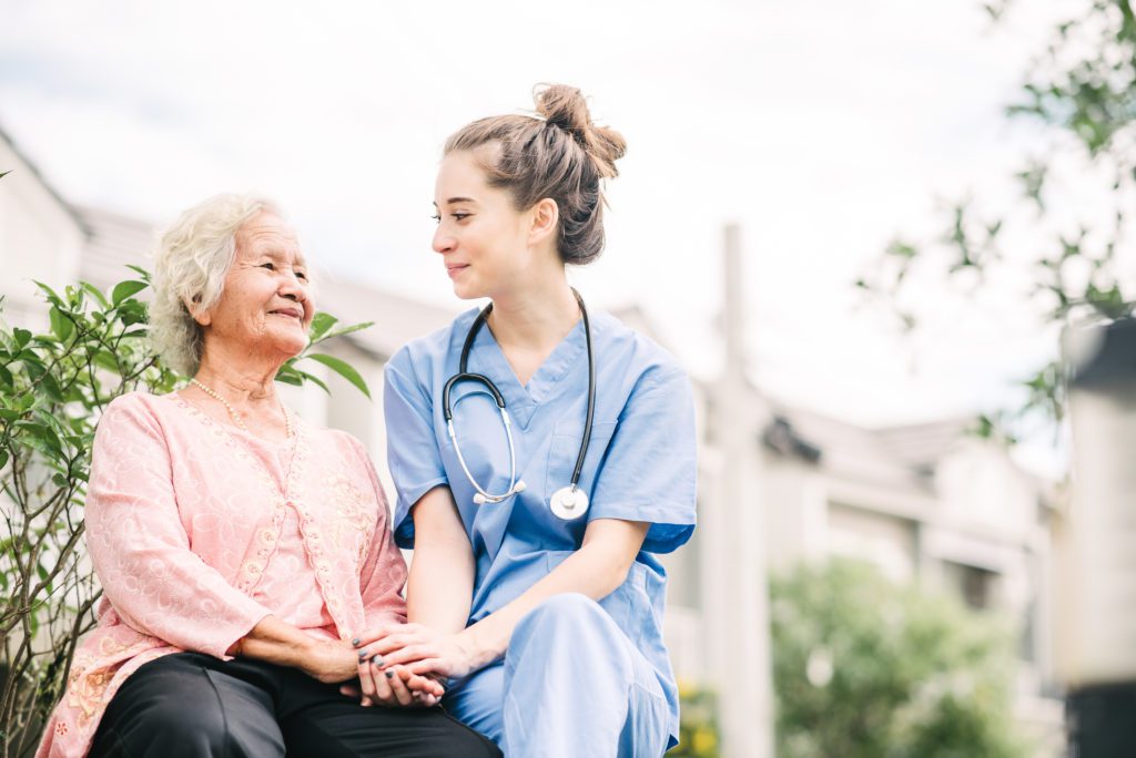 smiling nurse holding hand of happy elderly woman outdoor at the park