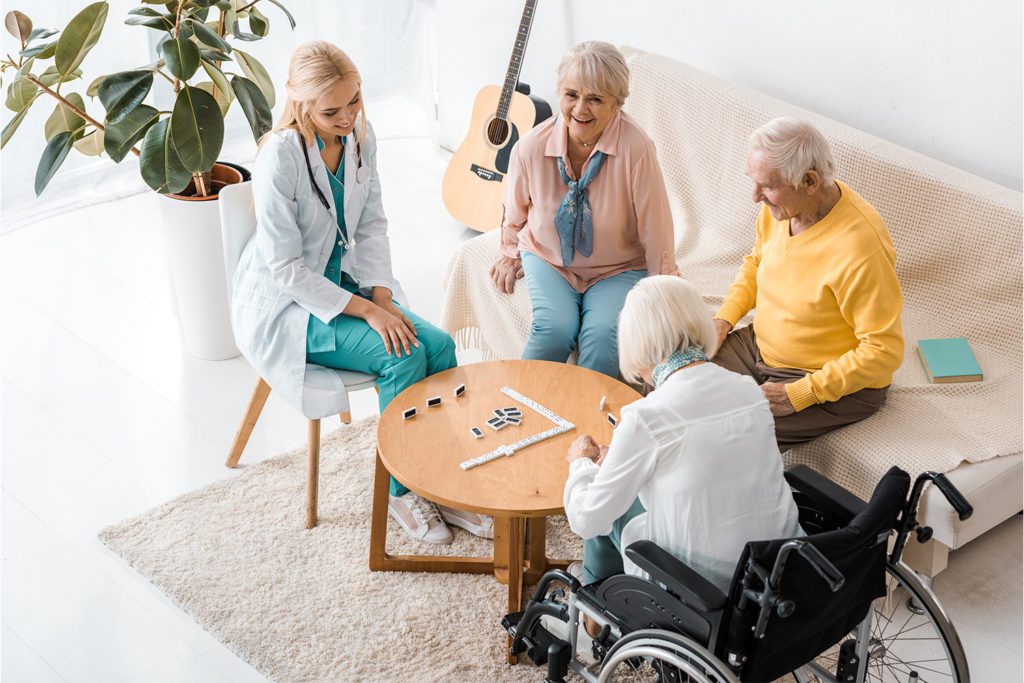Nurse and a group of elderly patients sitting down and playing dominoes at a skilled nursing facility