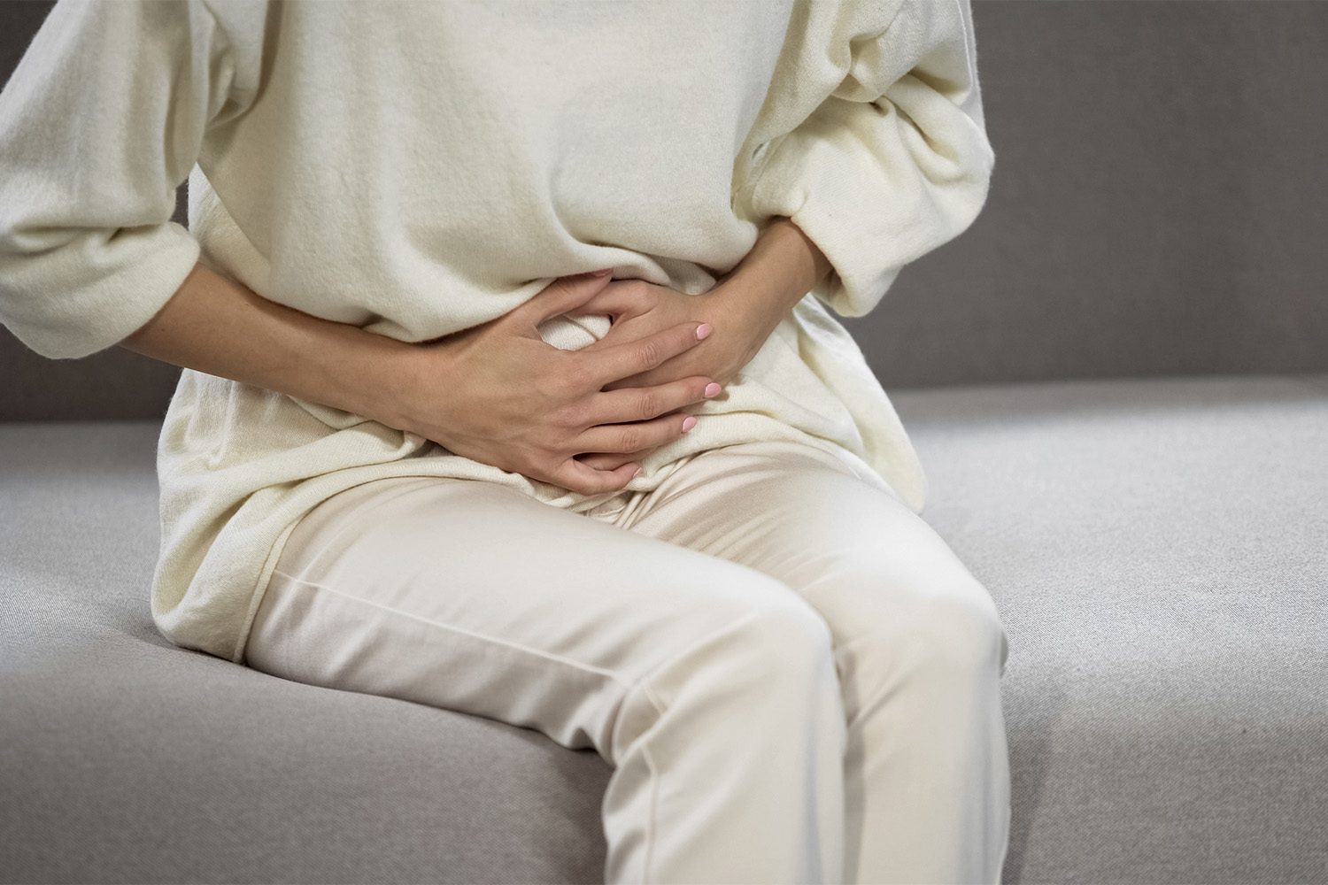 women sitting on a couch grabbing her abdomen as she's experiencing bladder spasms